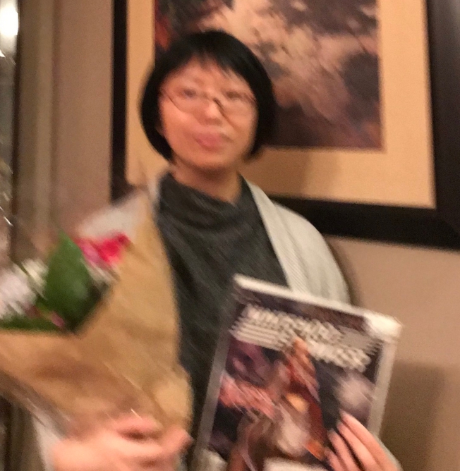 me (cool black turtleneck and grey cardigan) holding a bouquet of flowers and a copy of nintendo power with a lovely princess katia from lost kingdoms on the front. in the back is a framed painting on the wall of our house. the image is very blurry